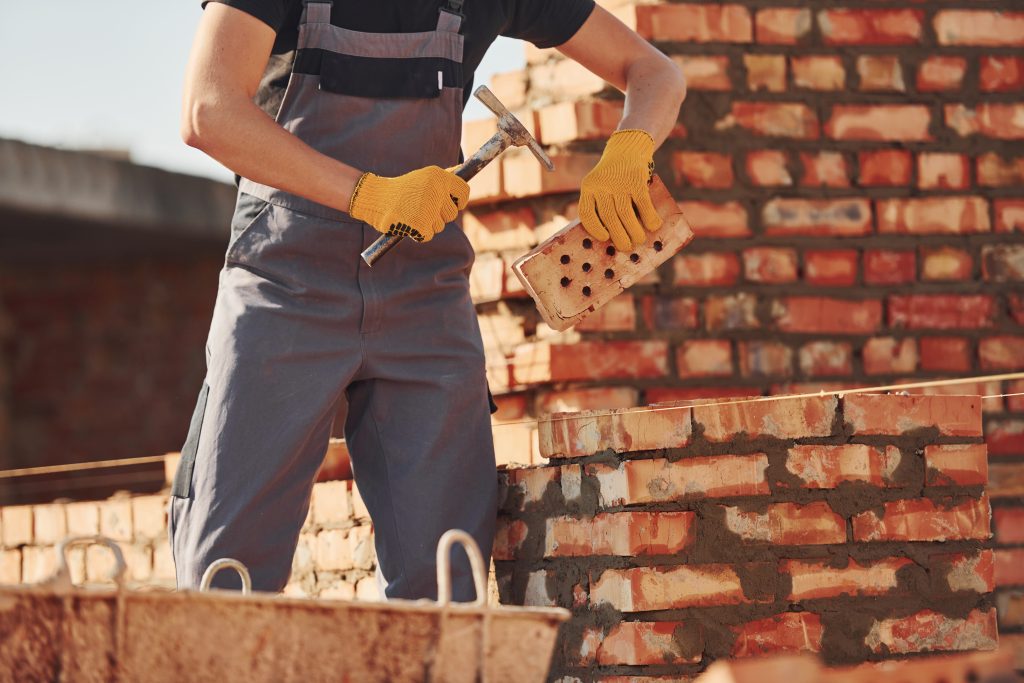 A man in overalls skillfully lays bricks on a wall, demonstrating his masonry expertise and craftsmanship.