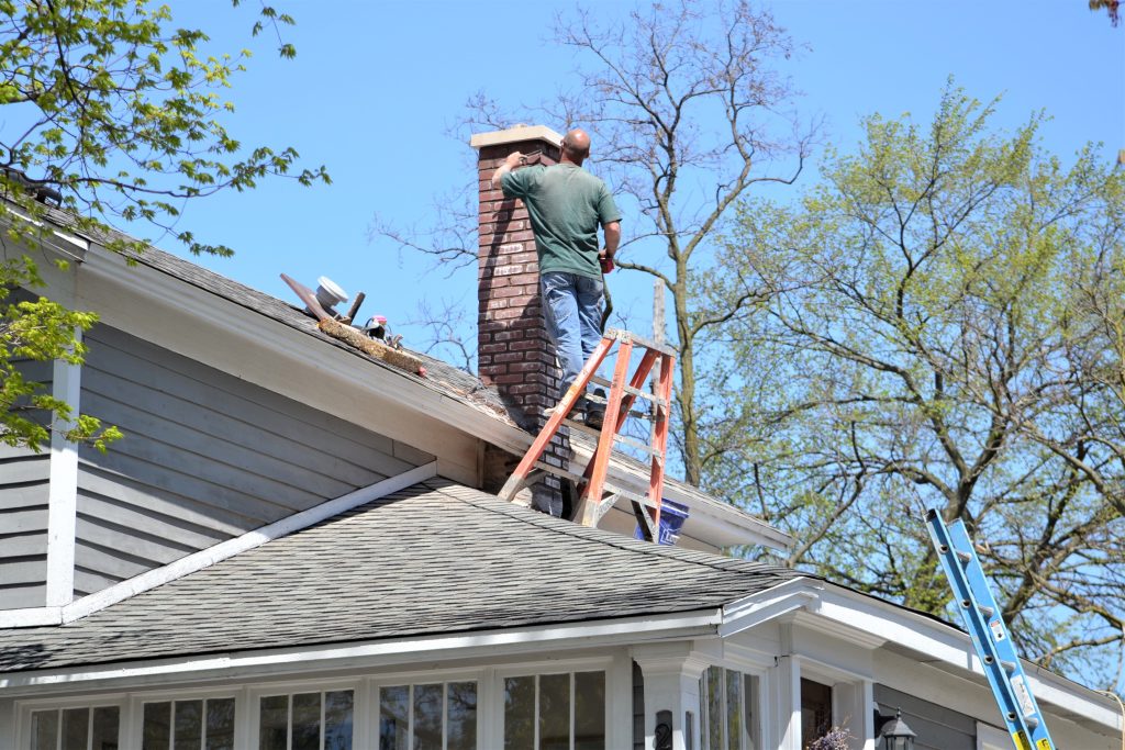 A man on a ladder performing chimney service, ensuring proper maintenance and safety for the home.