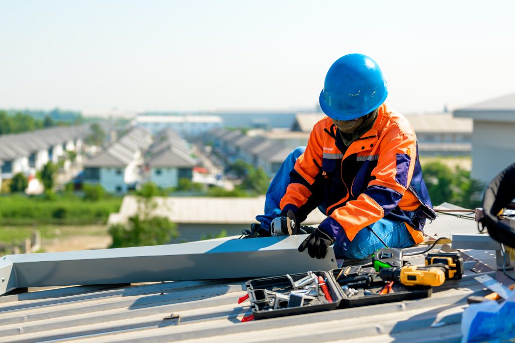 A man in an orange and blue jacket performs gutter service while working on a roof top