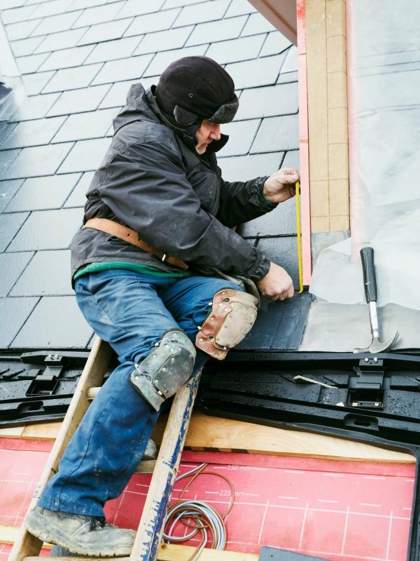 A man on a ladder performing chimney service work on a roof, ensuring safety and maintenance of the structure.