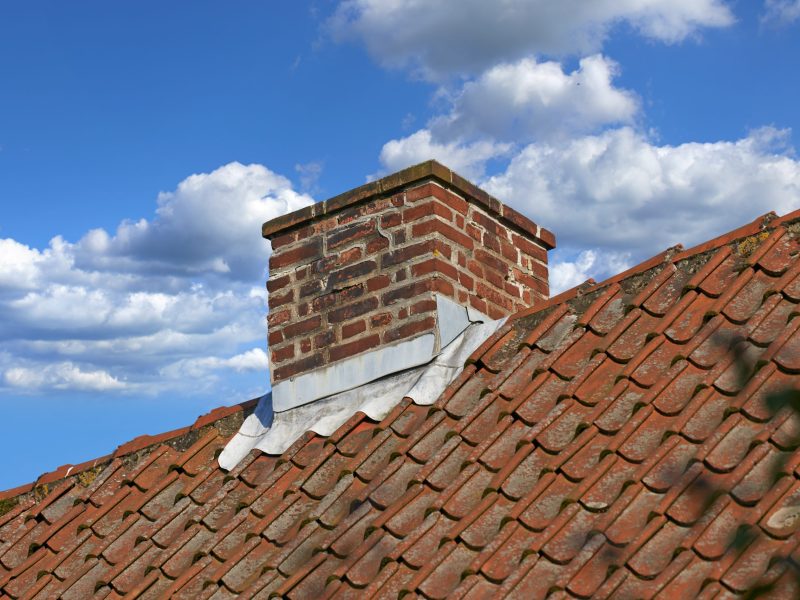 A brick chimney rising from a rooftop, surrounded by a clear blue sky, showcasing traditional architectural design.