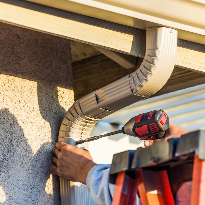 A man repairing a gutter on a house, demonstrating professional gutter service and maintenance expertise.